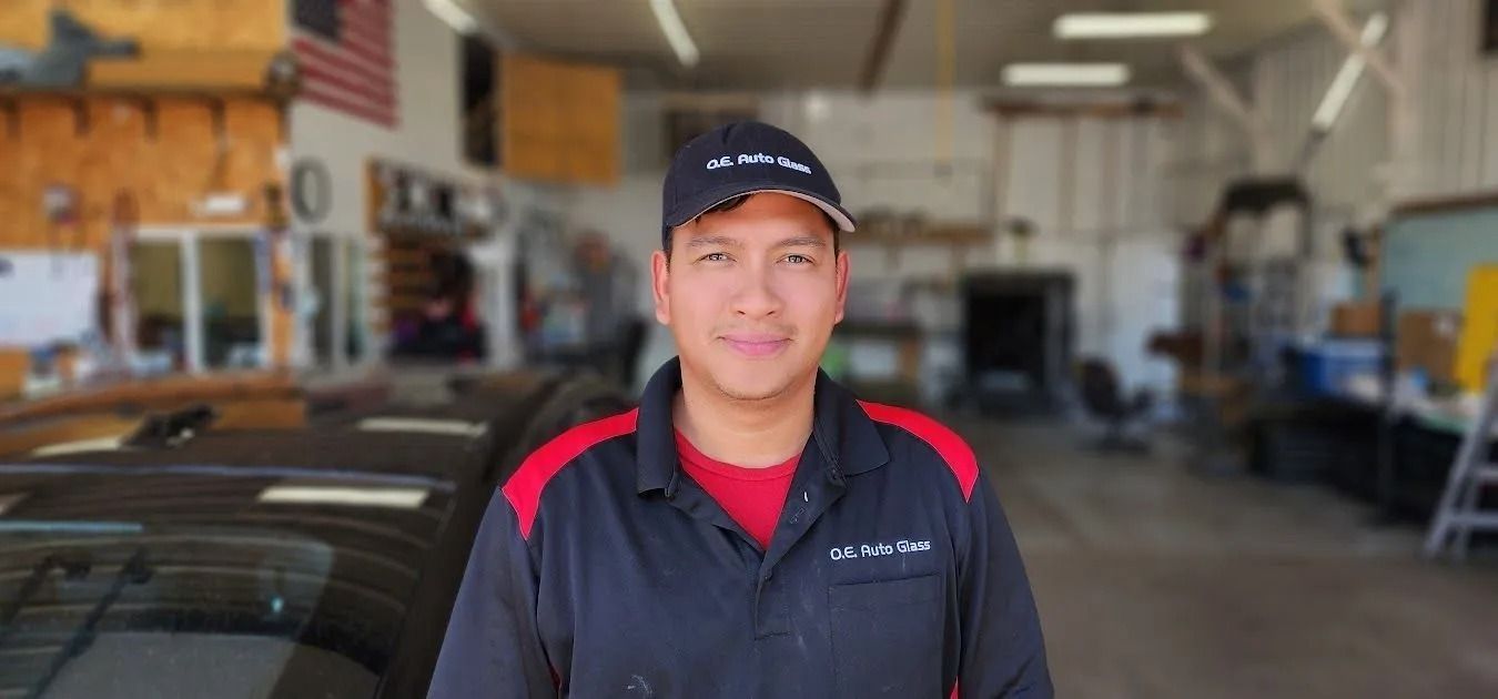 A person in a dark uniform with red accents and a black cap smiles in an auto repair shop.