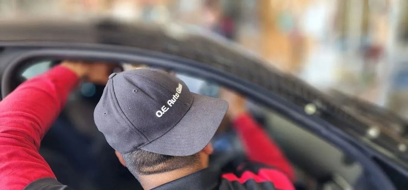 A person wearing a grey cap with an embroidered logo works inside the open driver-side window of a dark car.