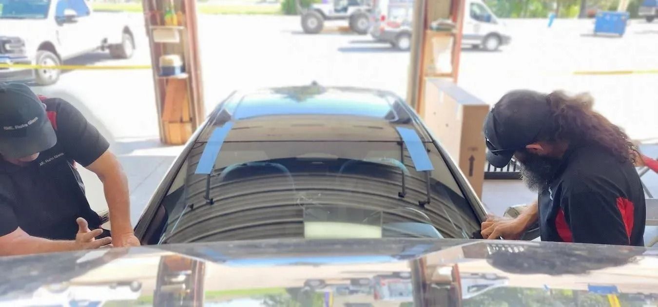 Two technicians in black uniforms work on a car’s windshield inside an automotive shop.
