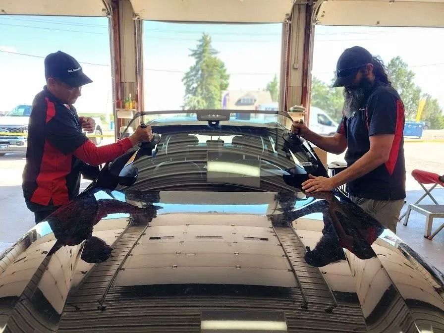 Two technicians in a garage use suction cups to carefully install a new windshield on a vehicle.