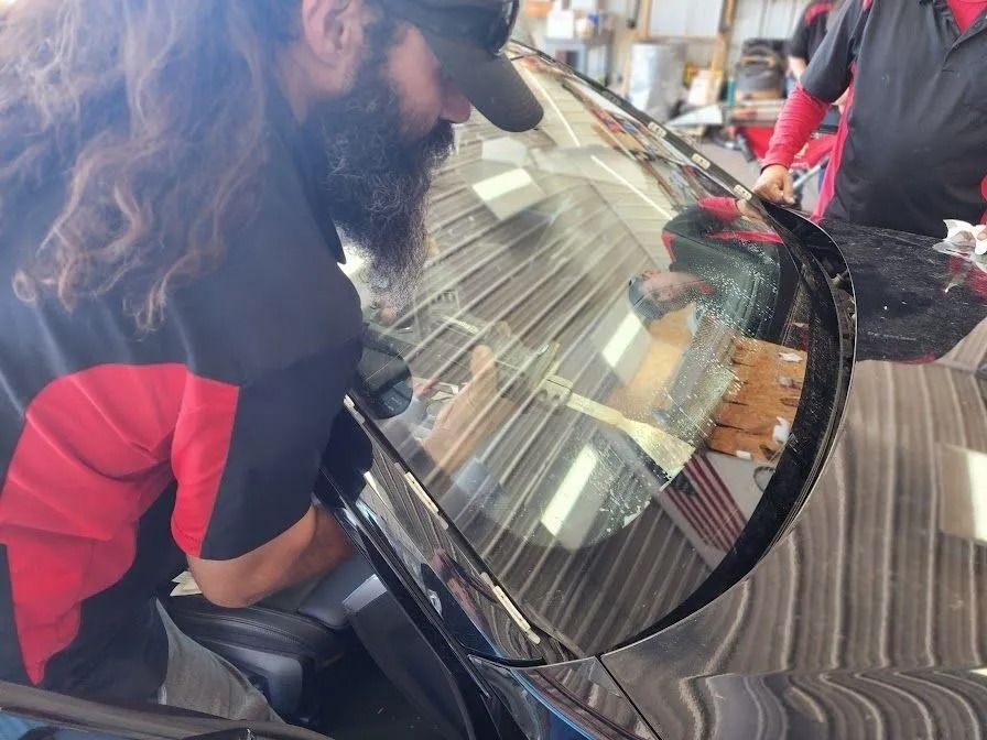 A technician in a red and black shirt replaces a cracked car windshield in a garage.