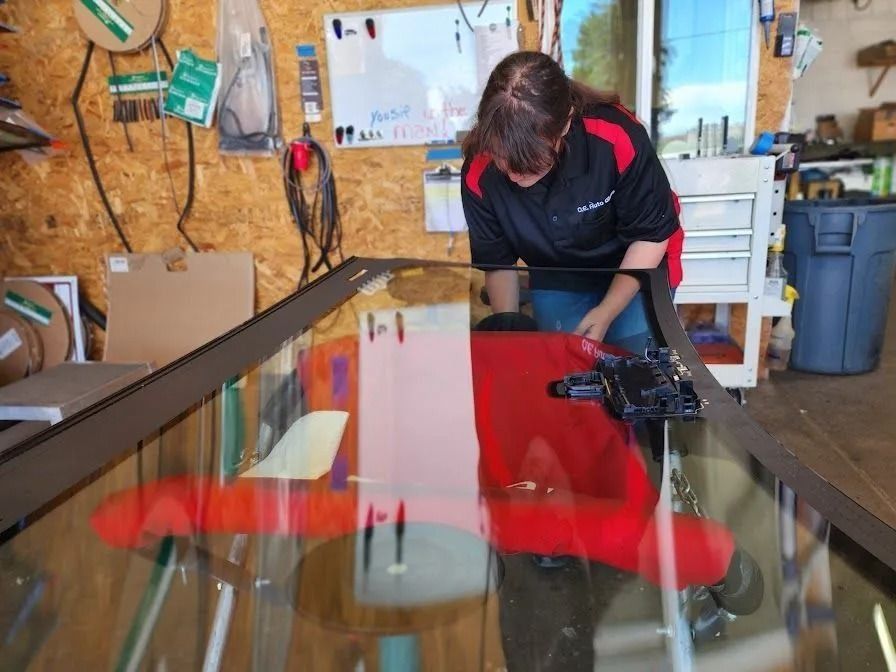 A person in a black and red uniform works on a large glass panel inside a workshop.
