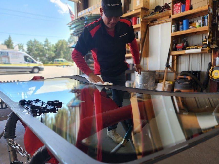 A person in a garage wiping down a large, framed glass windshield set on a workstation.