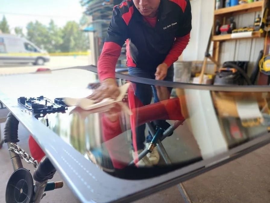A technician in a red and black uniform cleans a glass windshield in a workshop.
