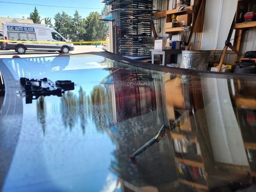 A large, curved automotive windshield reflects a parked van and the surrounding auto shop interior.
