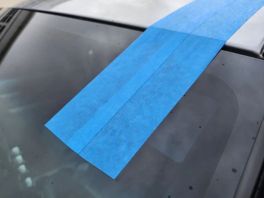 Two strips of blue painter's tape applied vertically to the top of a car's windshield.