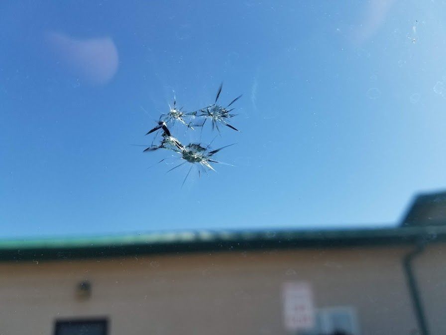 Two connected star-shaped cracks on a car windshield against a clear blue sky.