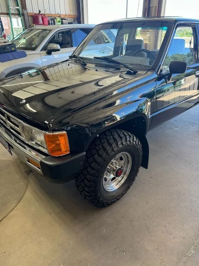 A shiny, black Toyota pickup truck with large, aggressive off-road tires parked inside a garage.