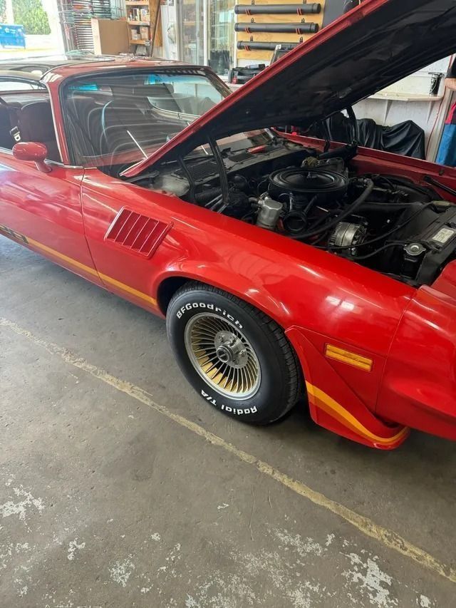 A bright red classic Pontiac Firebird with its hood open, parked inside a garage.