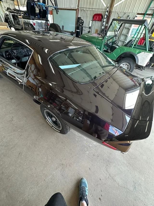 A high-angle view of a shiny black vintage muscle car in a garage, next to a green off-road vehicle.
