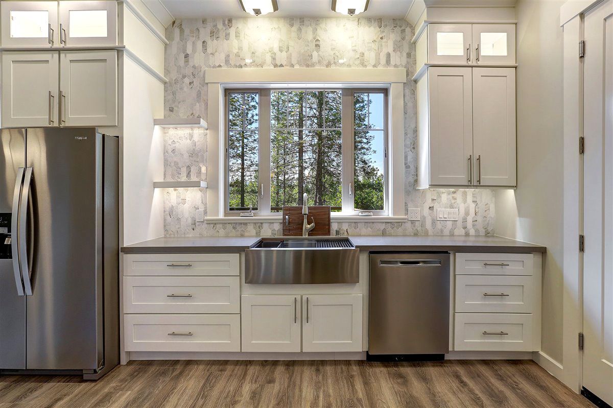 A kitchen with white cabinets , stainless steel appliances , a stove , sink , refrigerator and dishwasher.