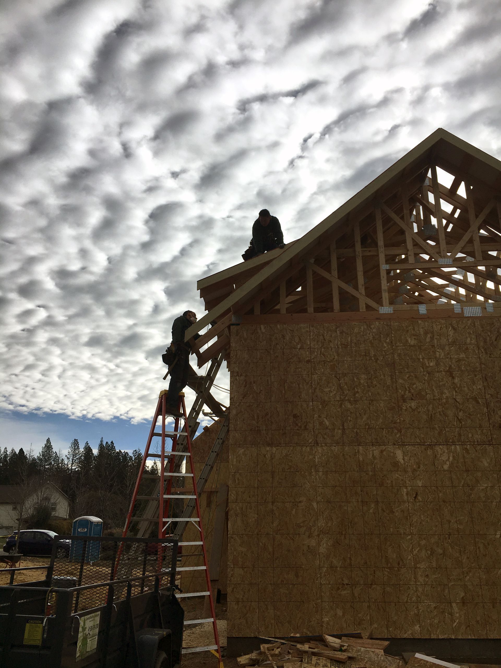A man on a ladder is working on the roof of a house under construction.