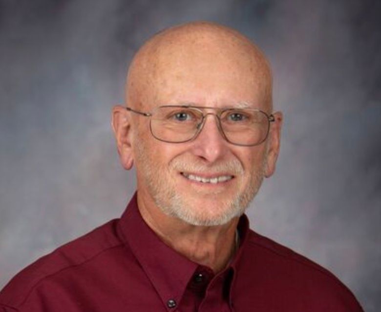 A bald man wearing glasses and a red shirt is smiling for the camera.