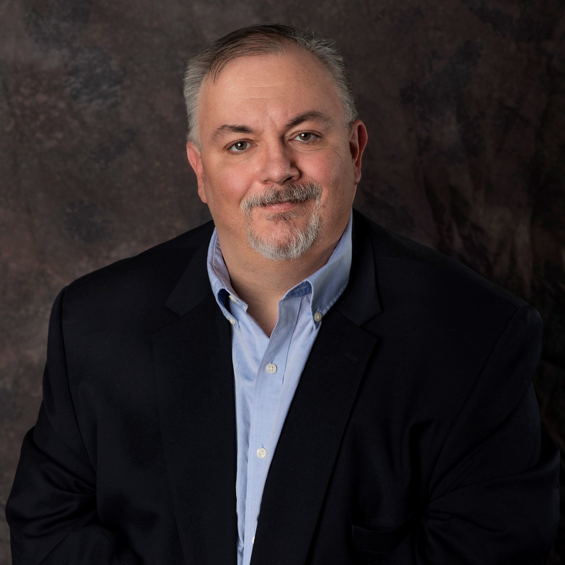 A man in a suit and blue shirt is smiling for the camera.