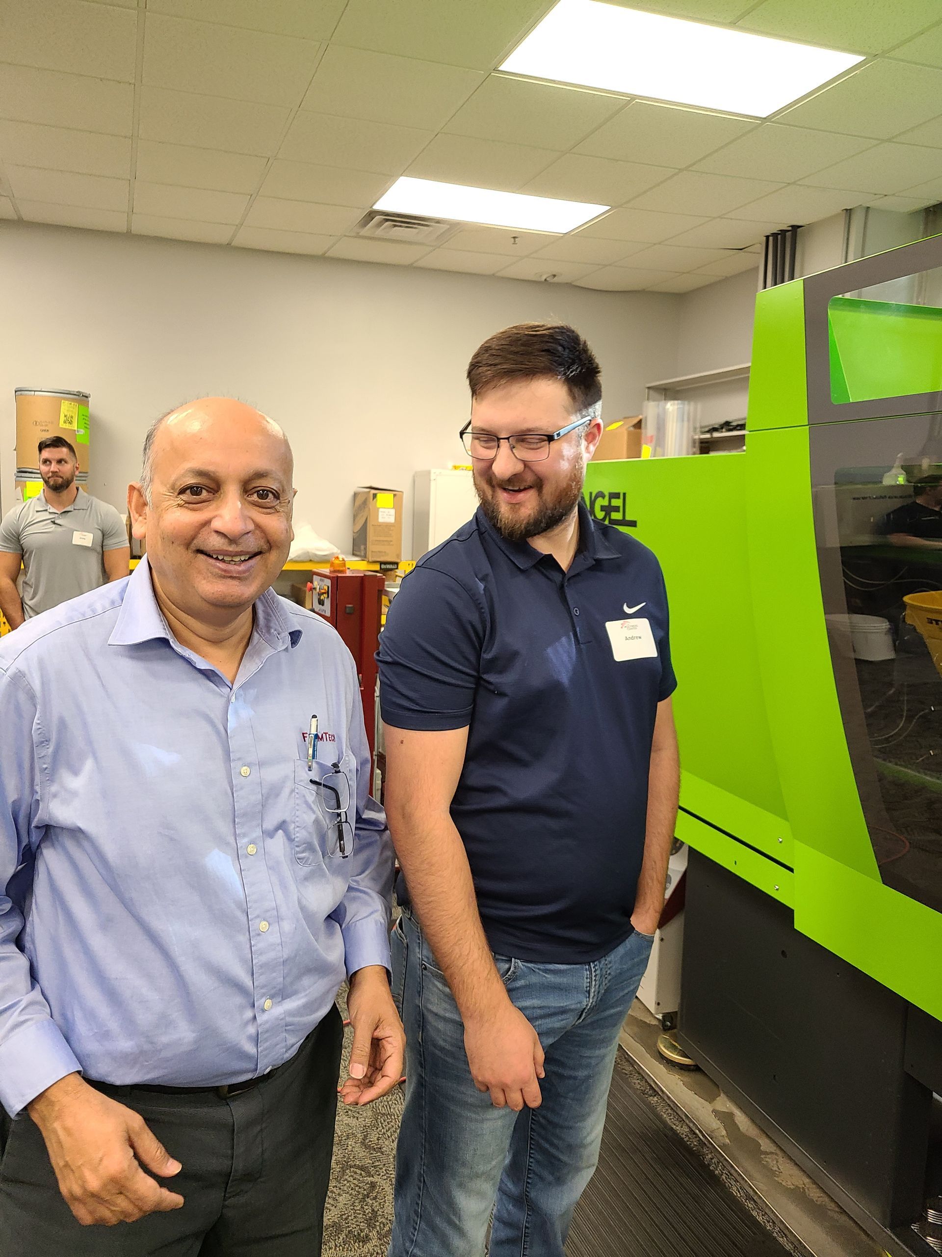 Two men are standing next to each other in a room in front of a green machine.