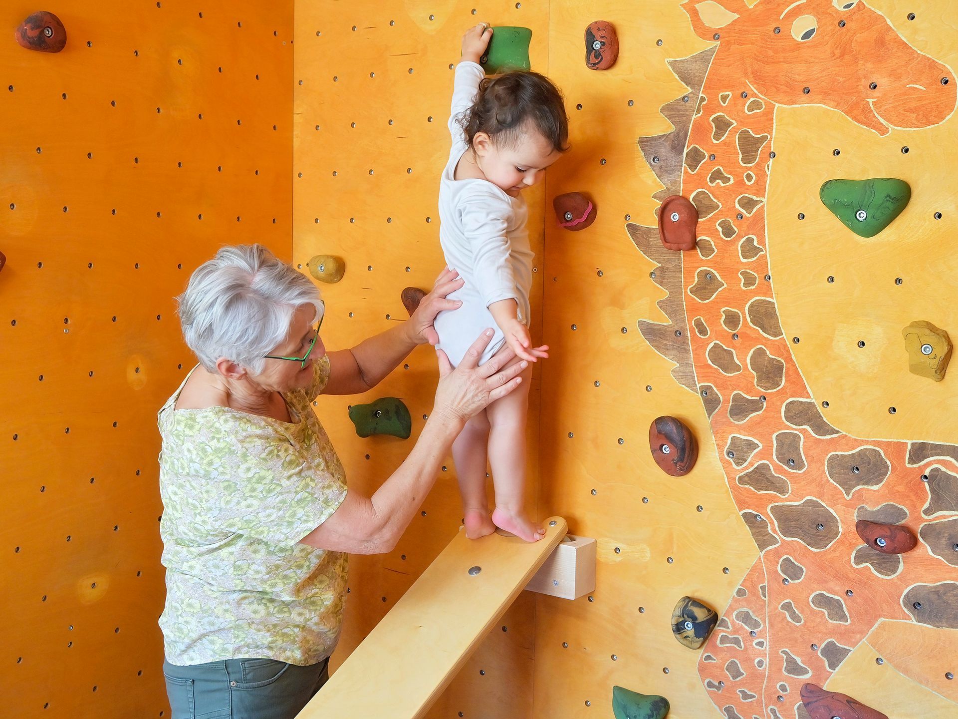 Eine Frau hilft einem kleinen Mädchen beim Erklimmen einer Kletterwand.