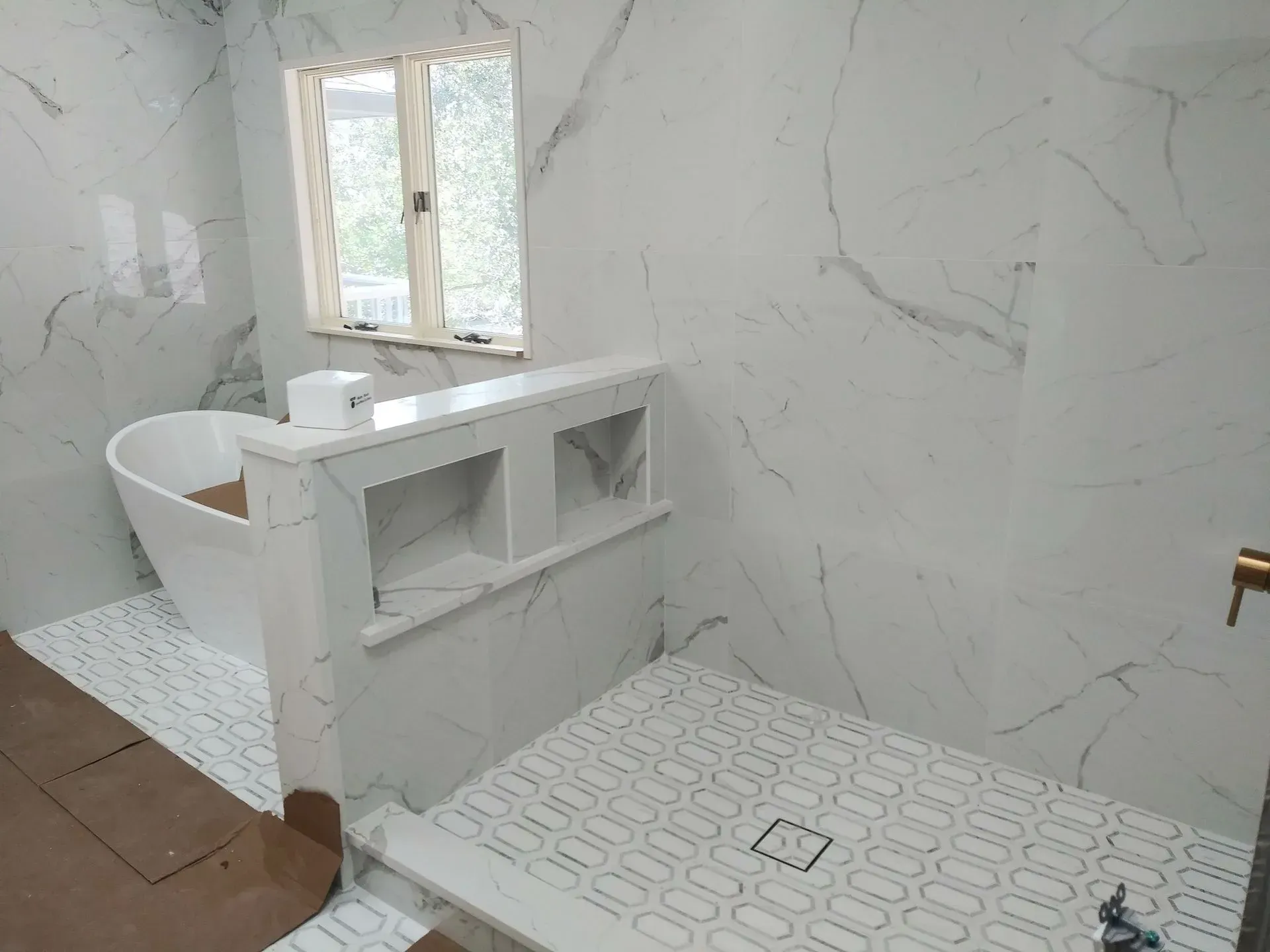 Bathroom with marble walls and floor, freestanding tub, shower with built-in shelves, and a window.