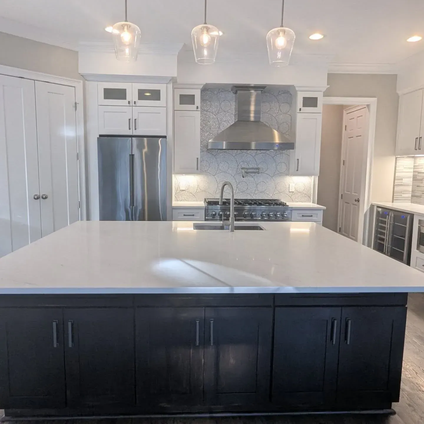 Modern kitchen with a dark island, stainless steel appliances, and white cabinets.