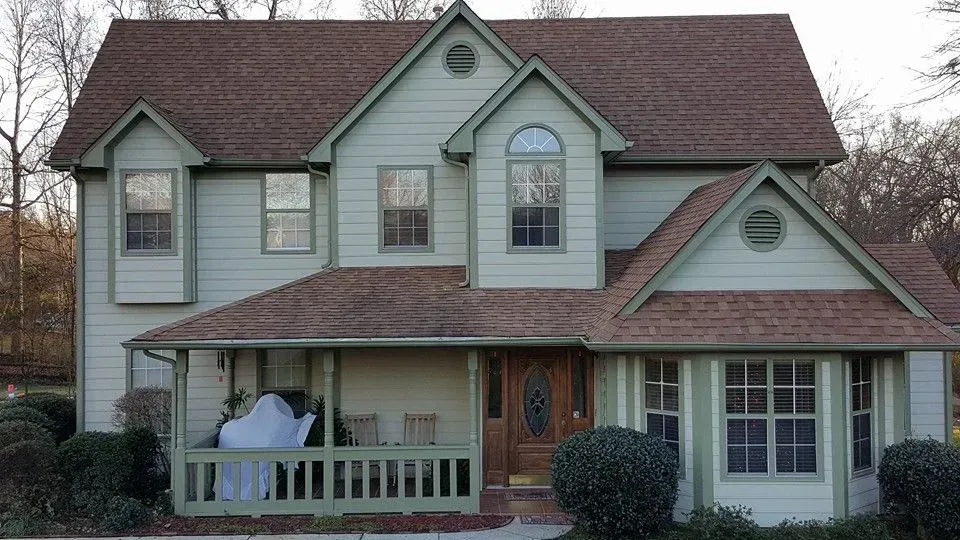 Two-story house with green siding, brown roof, and front porch.