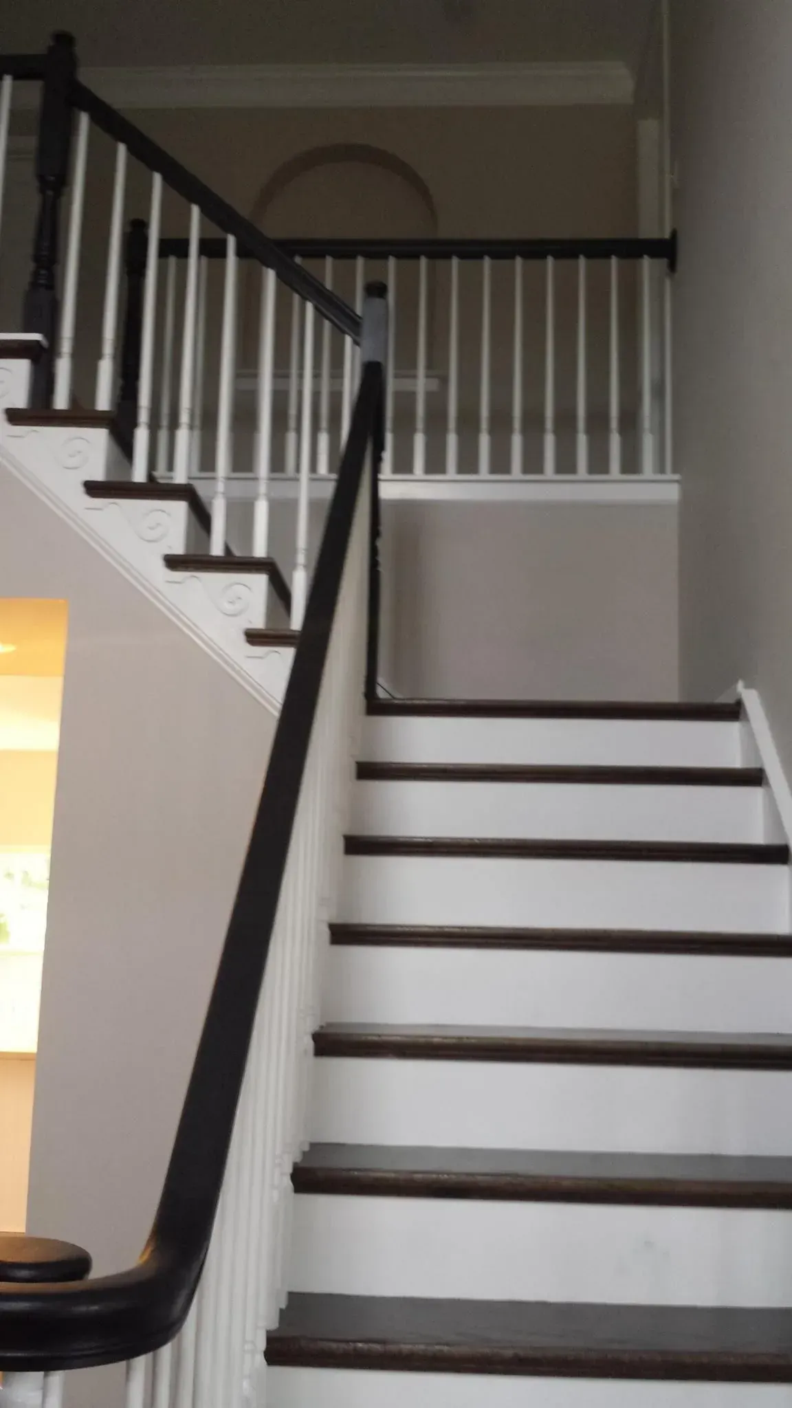Staircase with white steps and dark brown treads, leading upwards. Black handrail and white balusters.