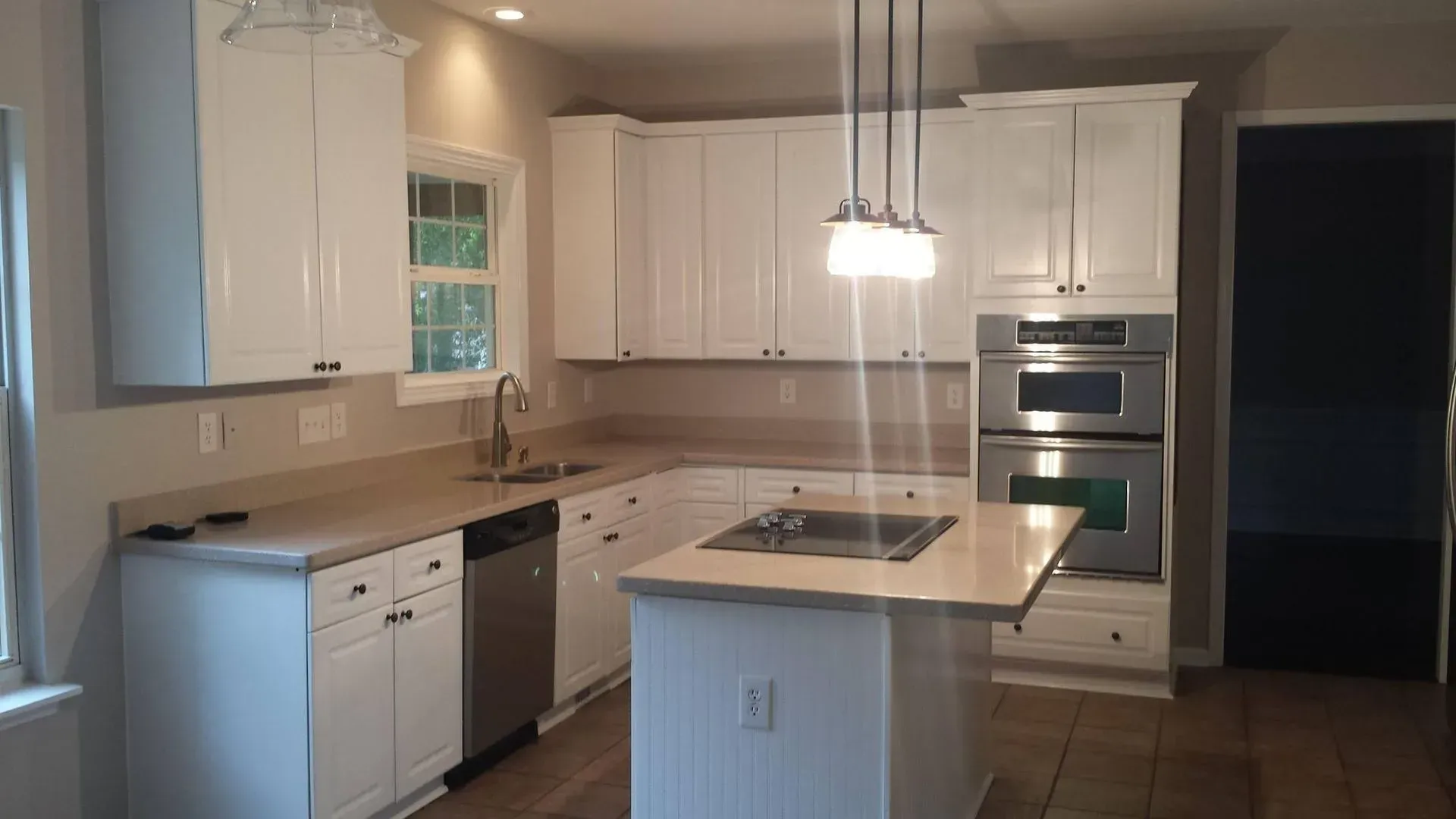 White kitchen with light countertops, stainless steel appliances, and island with stovetop.