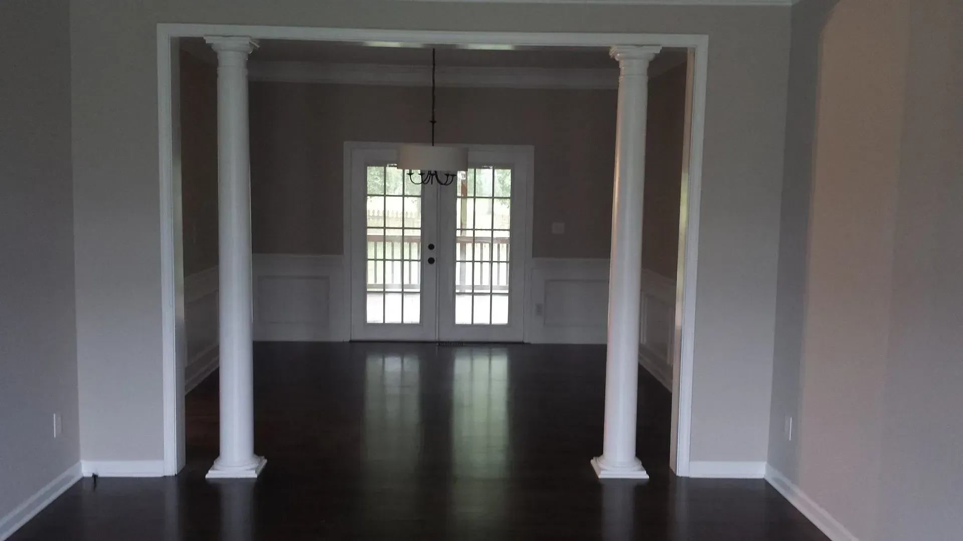 Interior view of a room with dark wood floors, white columns, and double doors in the distance.