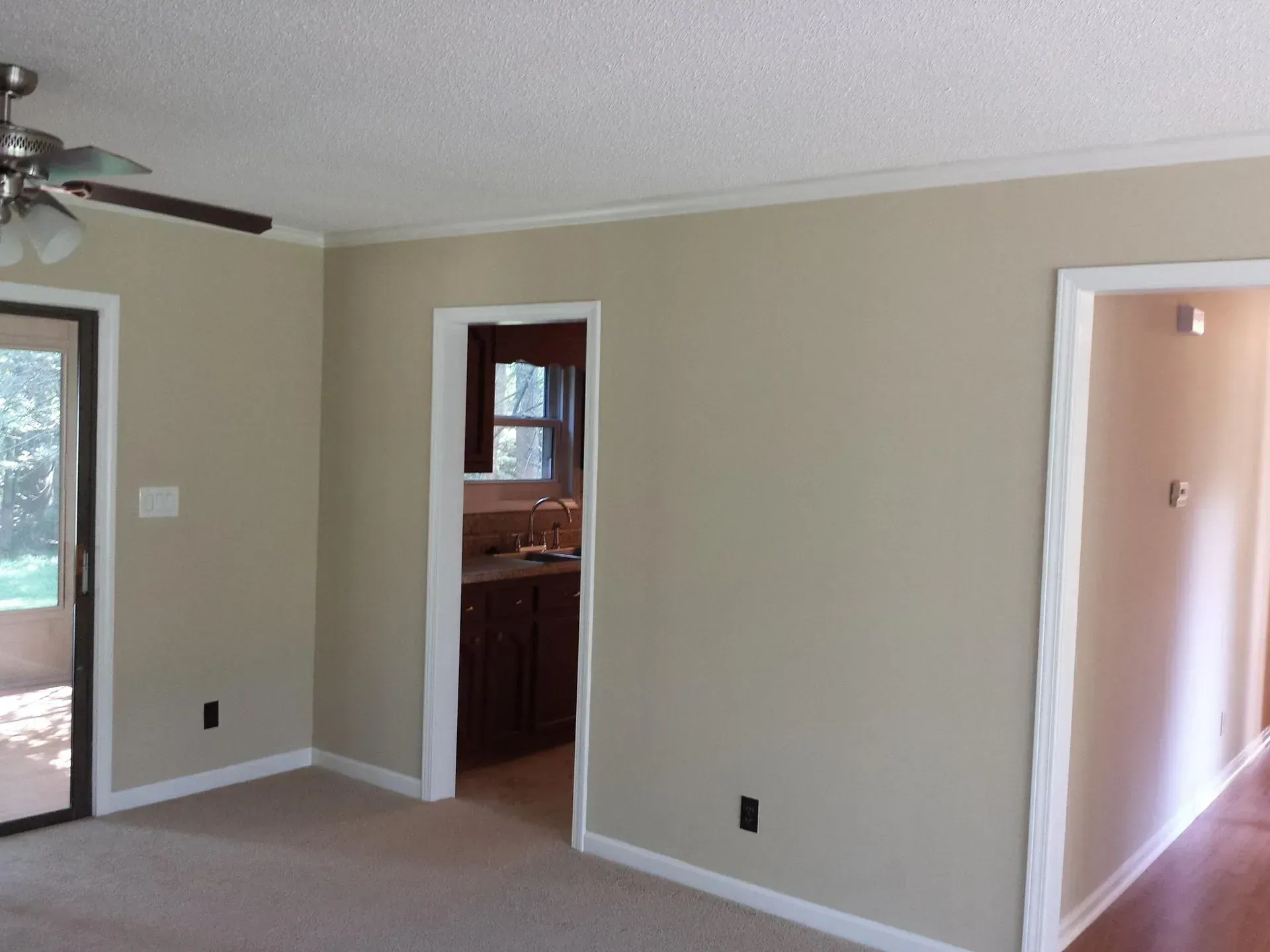 Beige-painted interior room with white trim, open doorways, sliding glass door, and a ceiling fan.