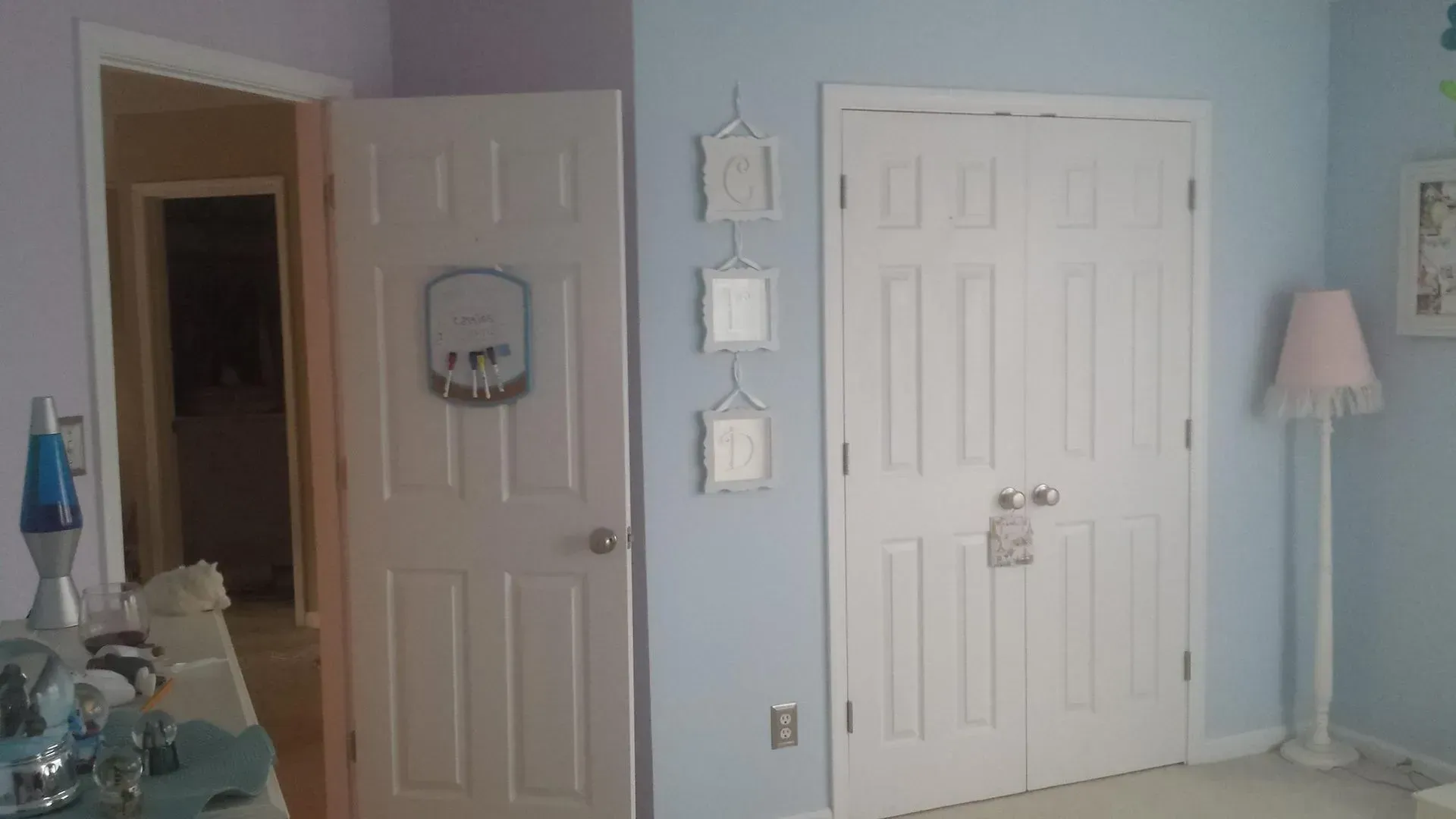 A room with light blue walls, a white closet, and a partially open door leading to another room.
