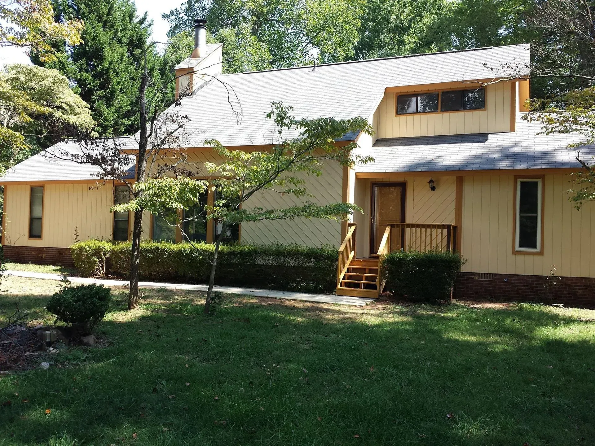 Yellow two-story house with brown trim and a green lawn. Trees and bushes surround the house.