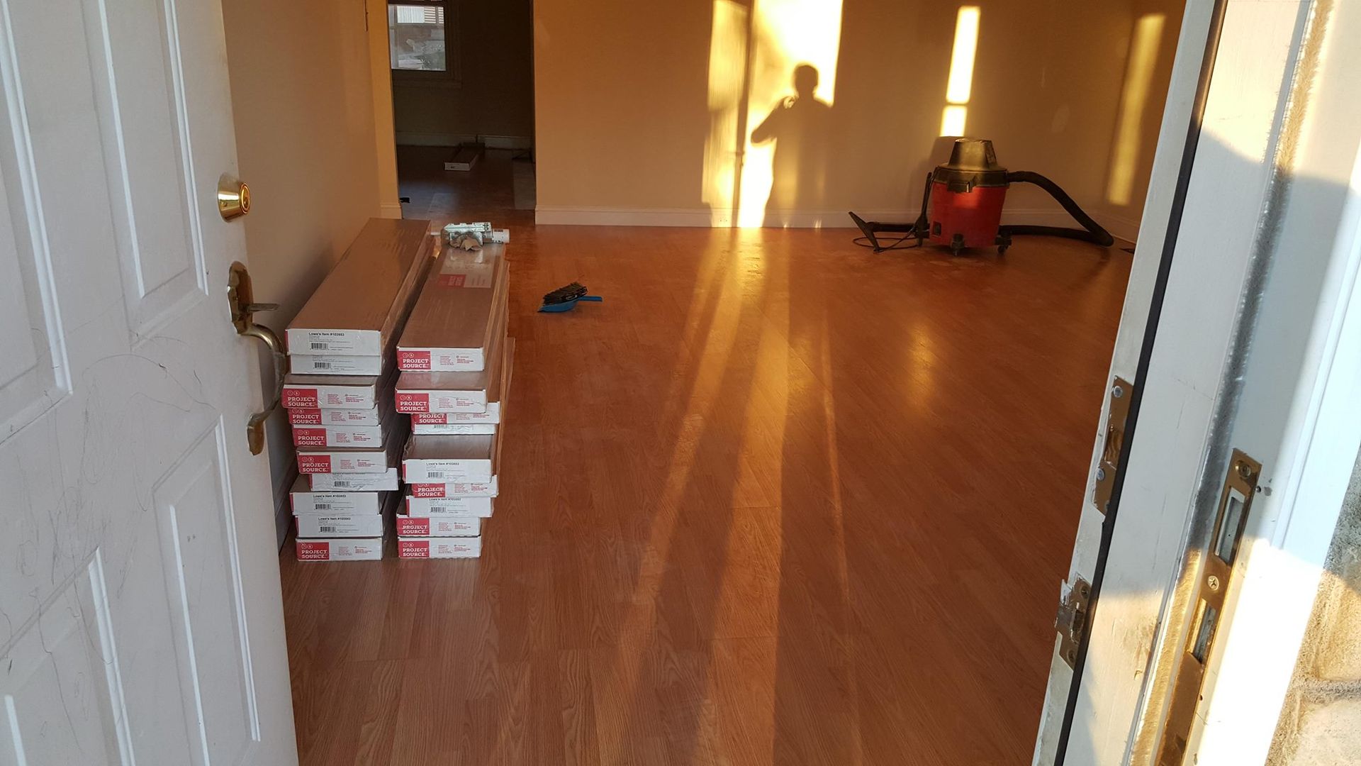 Open doorway to room with new wood flooring, boxes of flooring, and a person's shadow.
