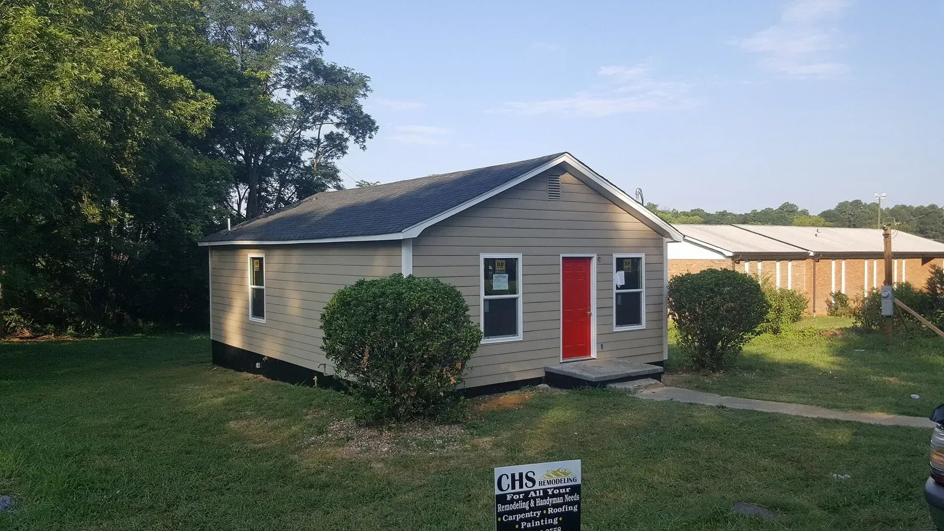 Small house with gray siding, red door, and bushes in front.