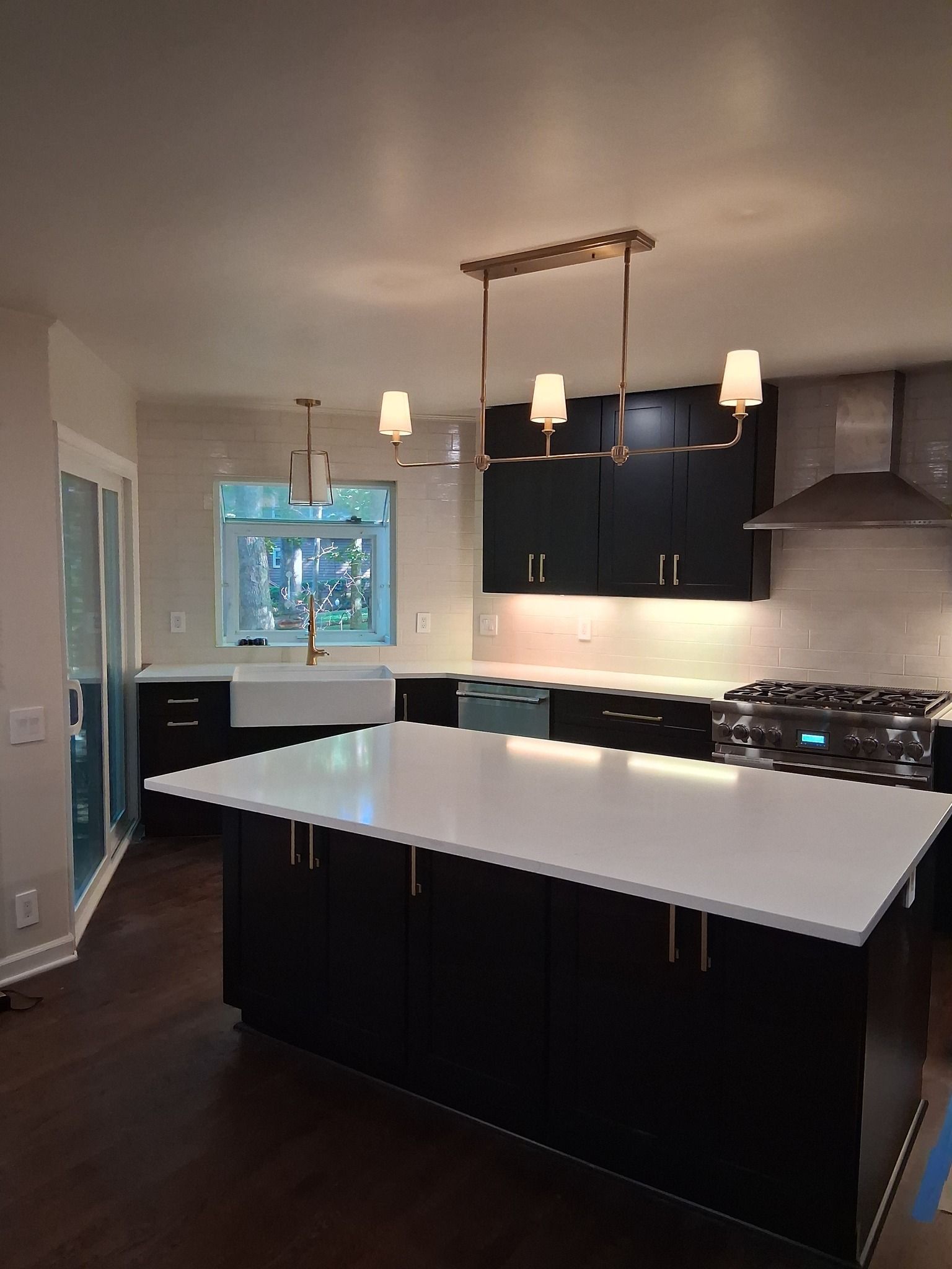 Modern kitchen with black cabinets, white countertops, and gold light fixtures.