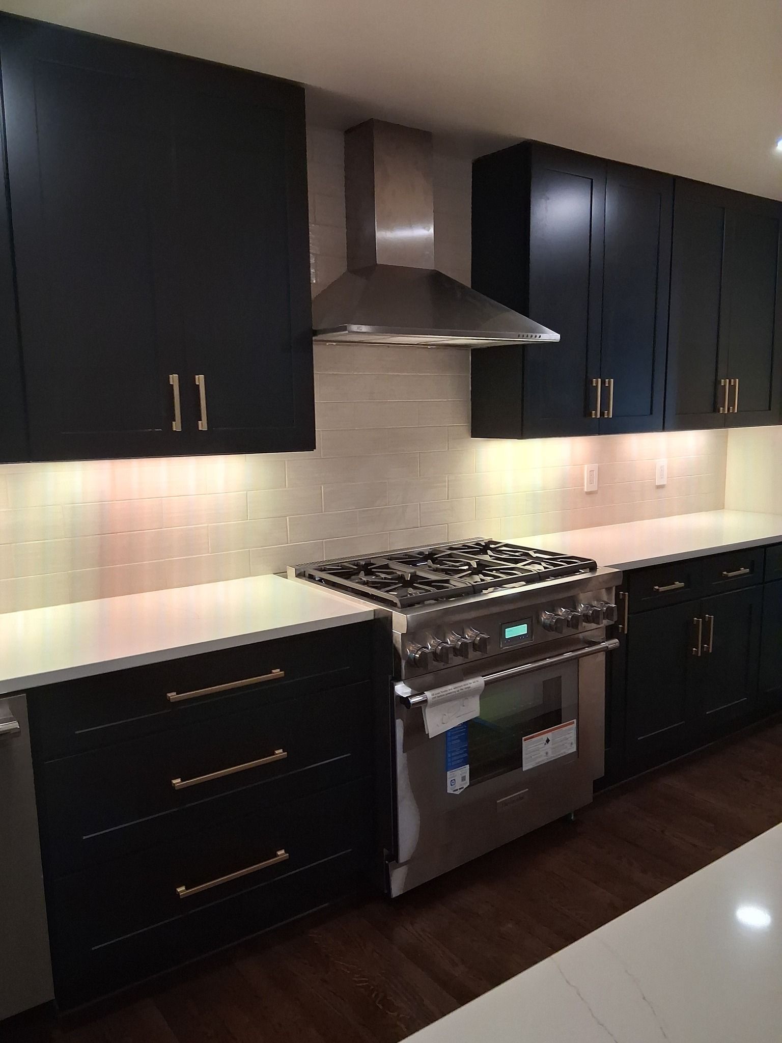Modern kitchen with black cabinets, stainless steel appliances, and white countertops.