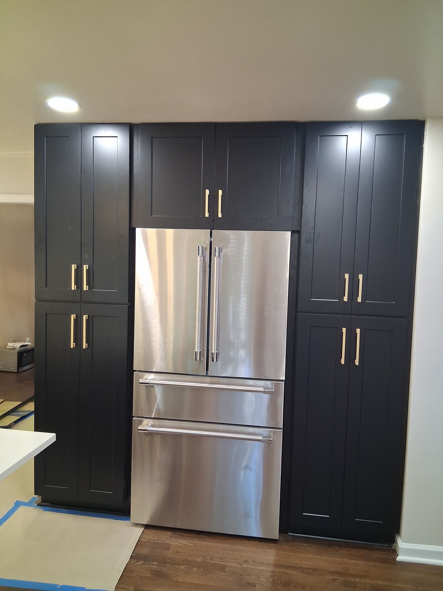 Stainless steel refrigerator flanked by black cabinets with gold handles in a kitchen.