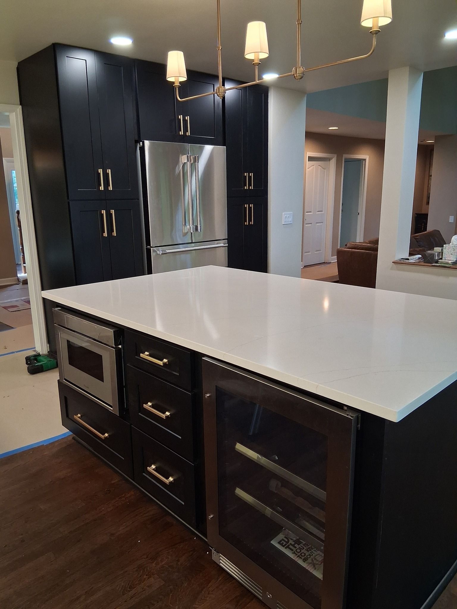 Modern kitchen with black cabinets, white countertop island, stainless steel appliances, and gold hardware.