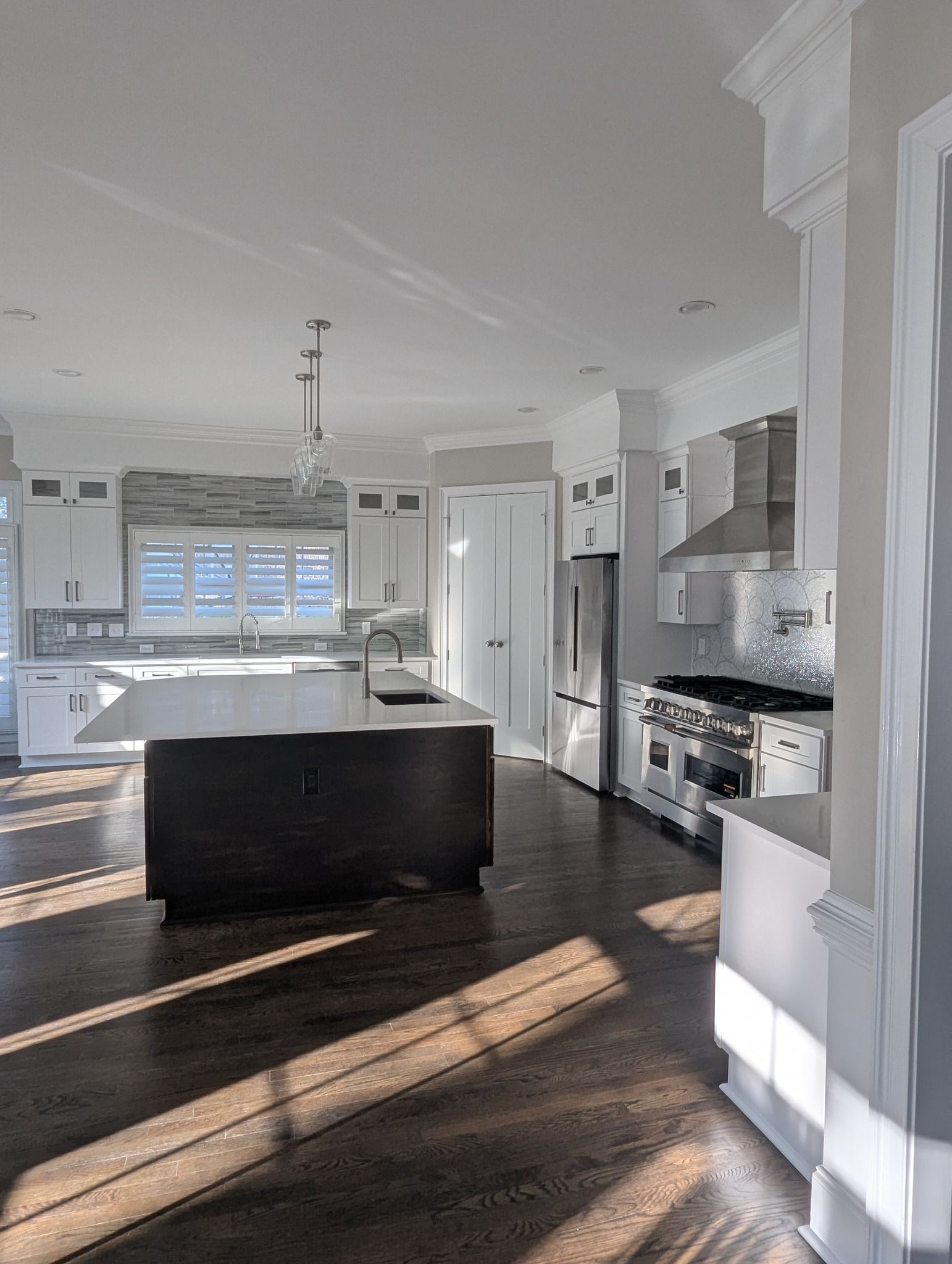 Bright, modern kitchen with dark wood floors, white cabinets, and a central island. Sunlight streams in.