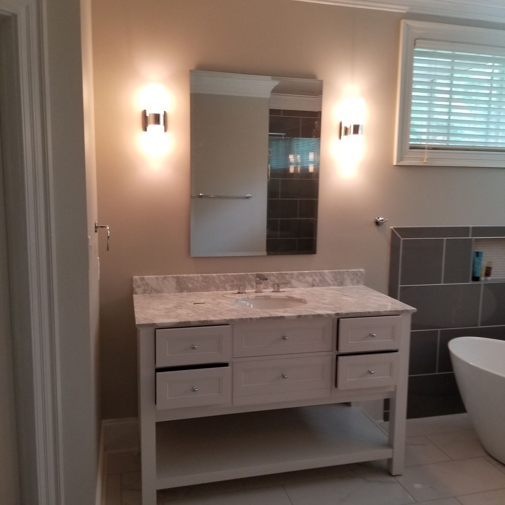 Bathroom with white vanity, marble countertop, mirror, sconces, and gray tile shower.