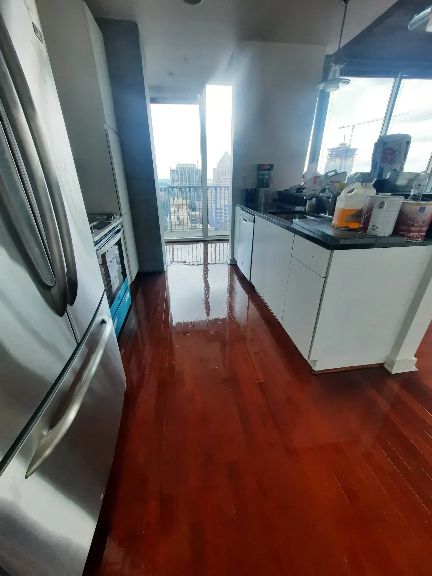 Red floor kitchen with stainless steel appliances, white cabinets, and a city view.