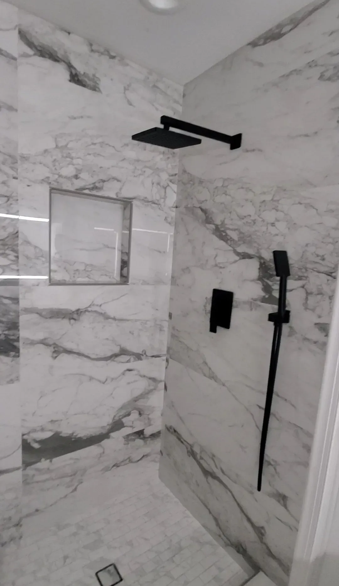 Modern shower with marble-look walls, black fixtures, and recessed shelf.