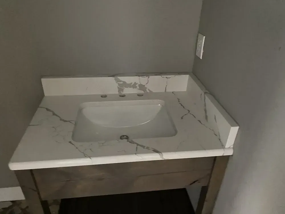 Vanity with white quartz countertop and integrated sink. The cabinet is dark wood.