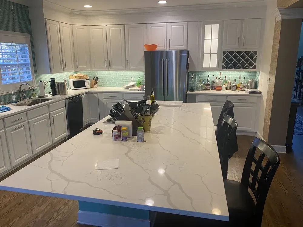 Kitchen with white cabinets, large island, stainless steel refrigerator, and wine rack.