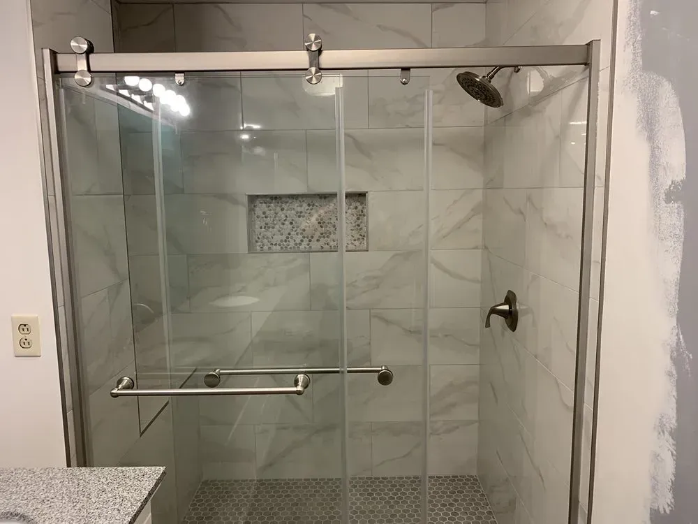Shower with glass doors and a stainless steel sliding bar. Marble-like tile lines the walls.