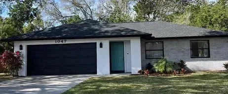 Gray house with black garage door, teal front door, and black-framed windows. Landscaping in front.