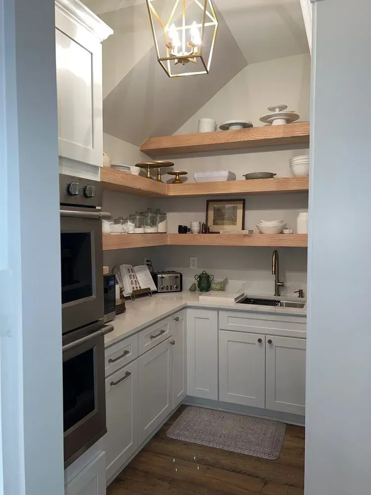 White kitchen with wood shelves, sink, and oven. A light fixture hangs from the angled ceiling.