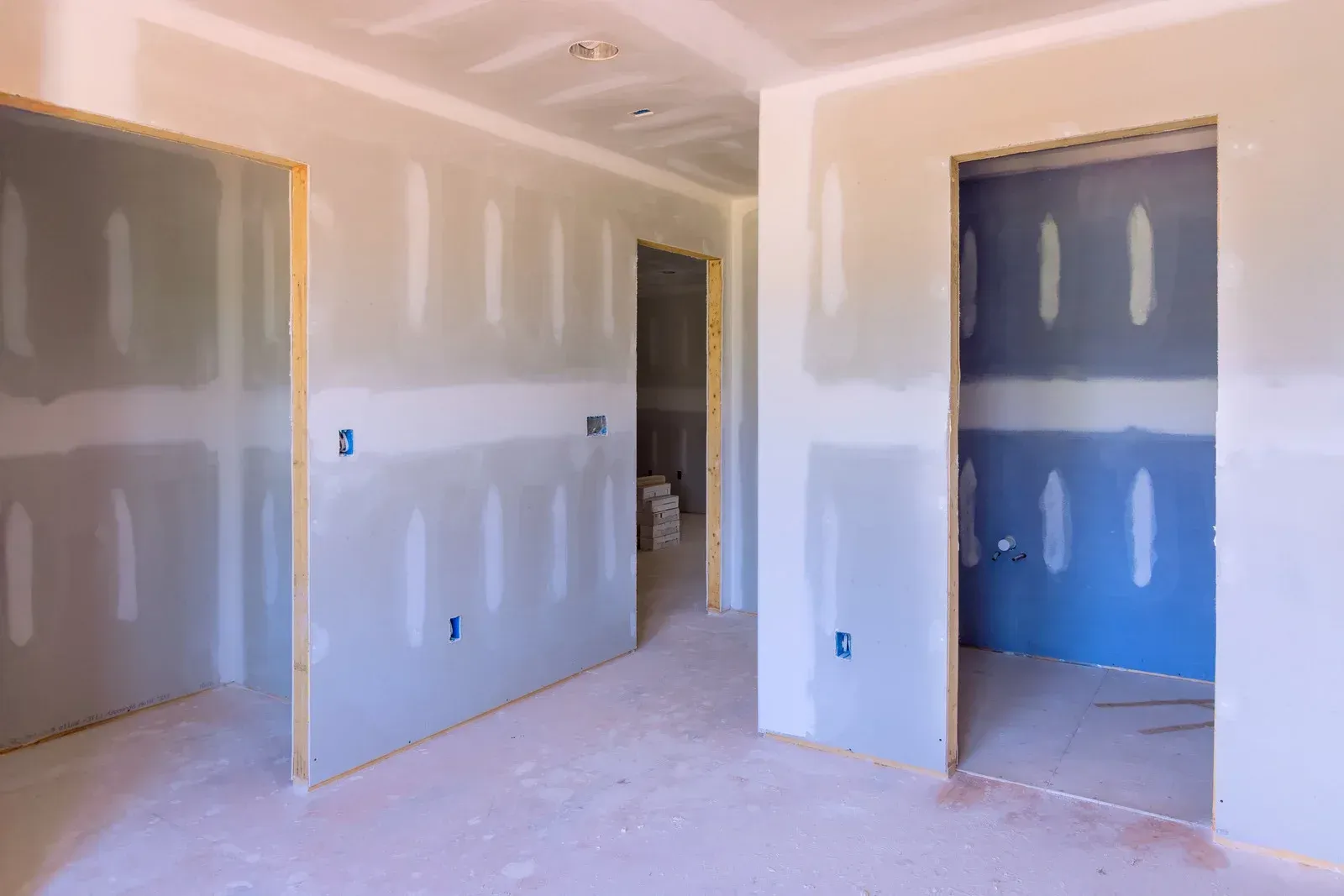 Interior view of a room under construction with drywall installed on walls and ceiling; doorways visible.