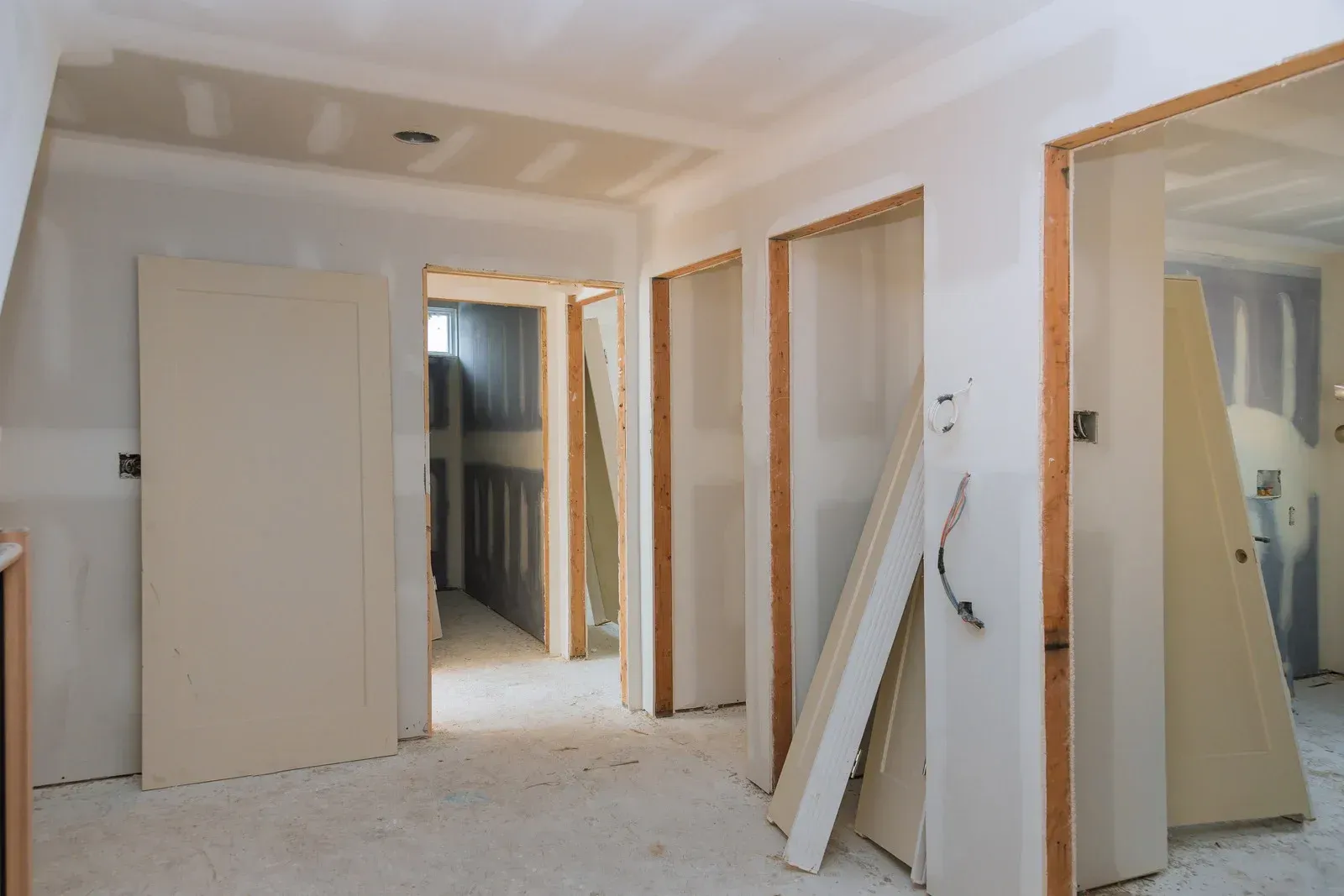 Interior hallway during renovation with open doorways, drywall, and stacked materials.