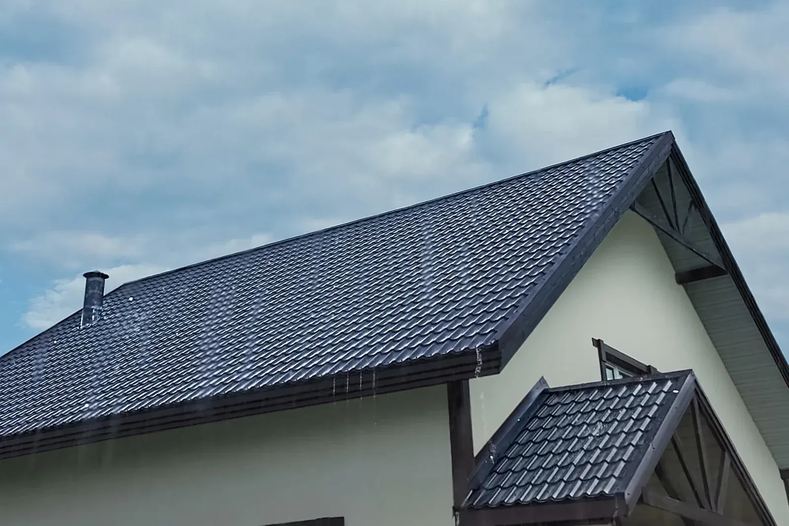 Dark gray tiled roof on a cream-colored building with dark brown trim, against a cloudy sky.