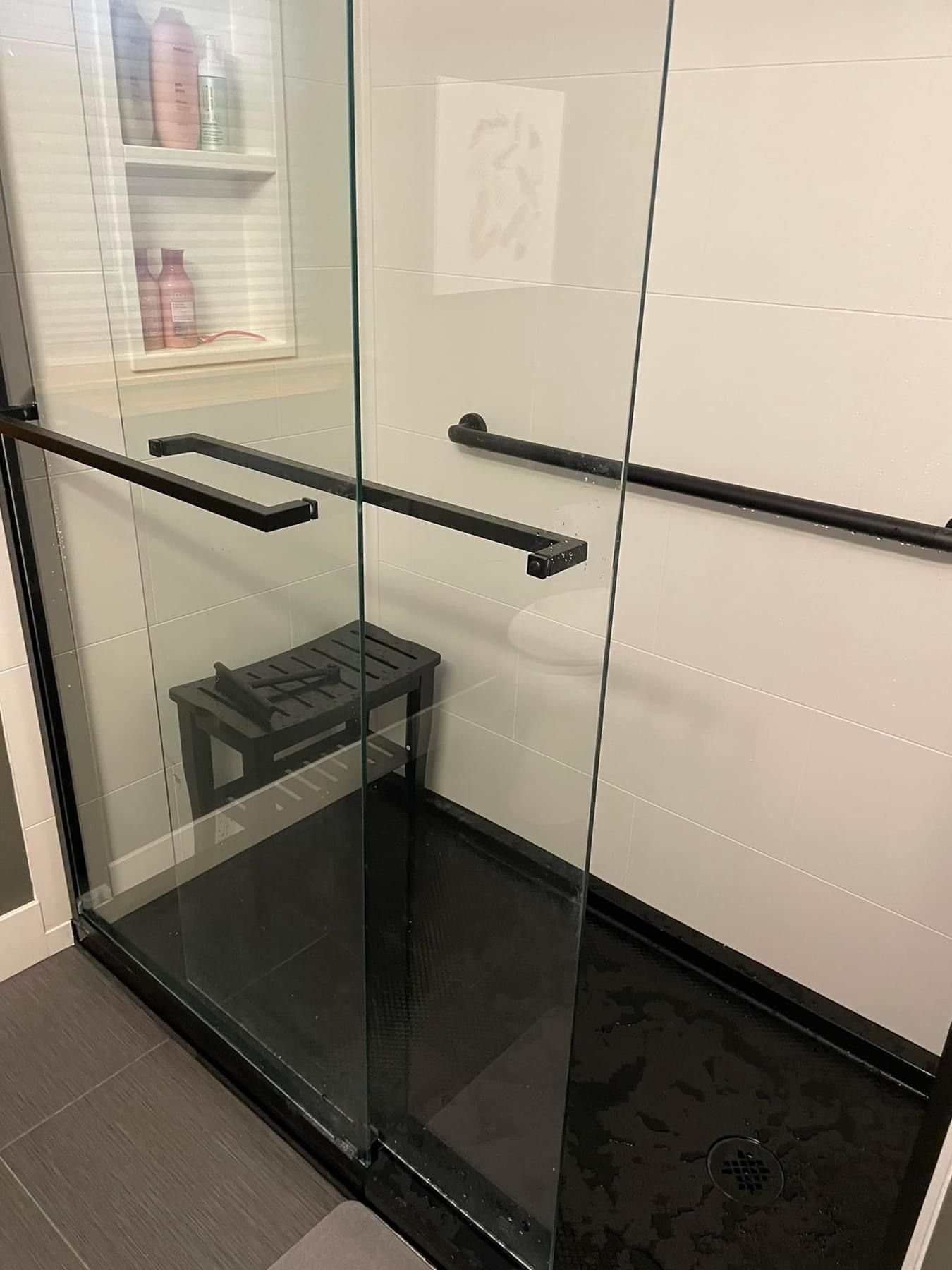 Modern shower with black frame, glass doors, and black bench. White walls, gray tile floor.