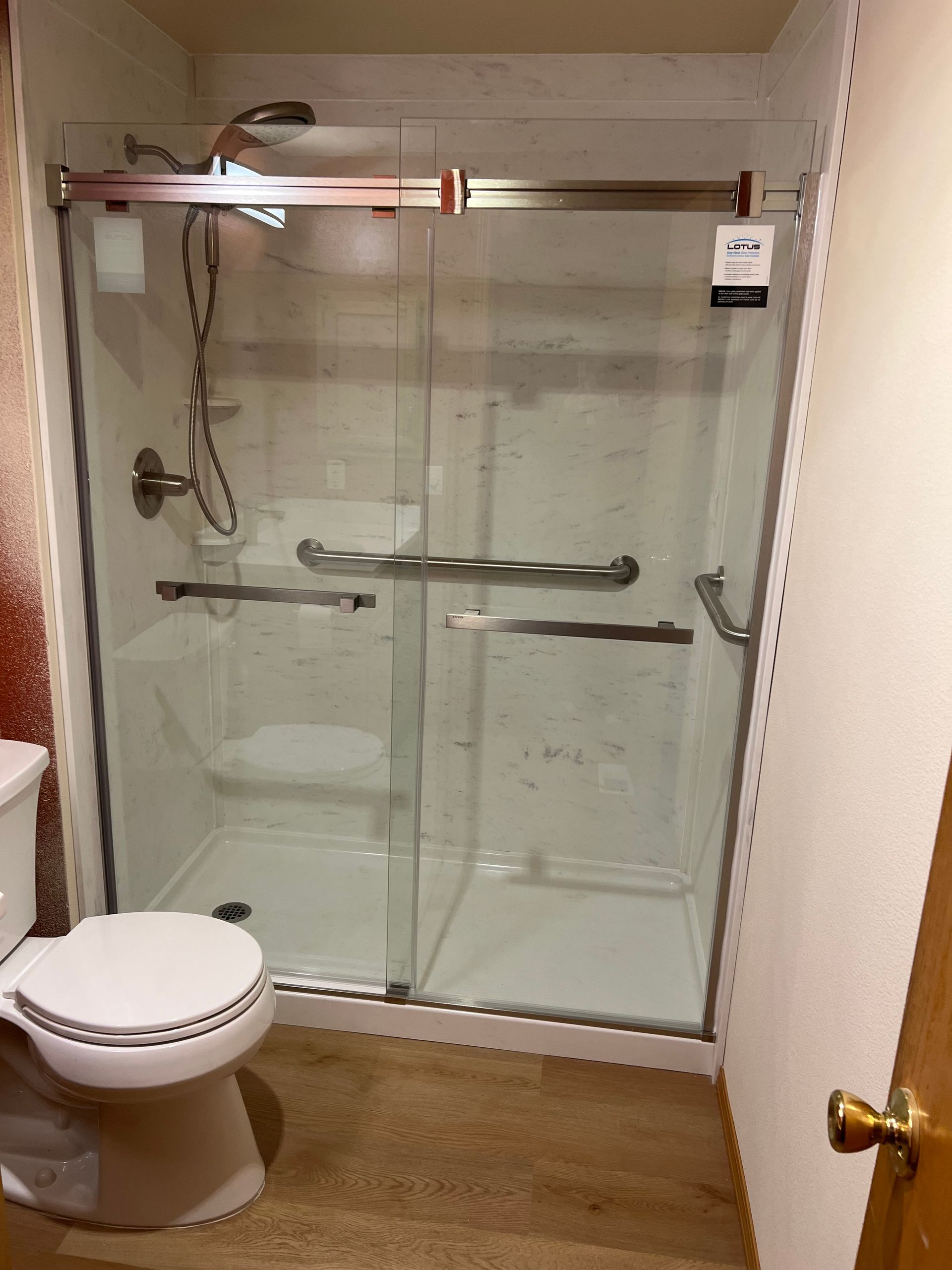 A clear glass shower with a sliding door and a toilet in a bathroom.