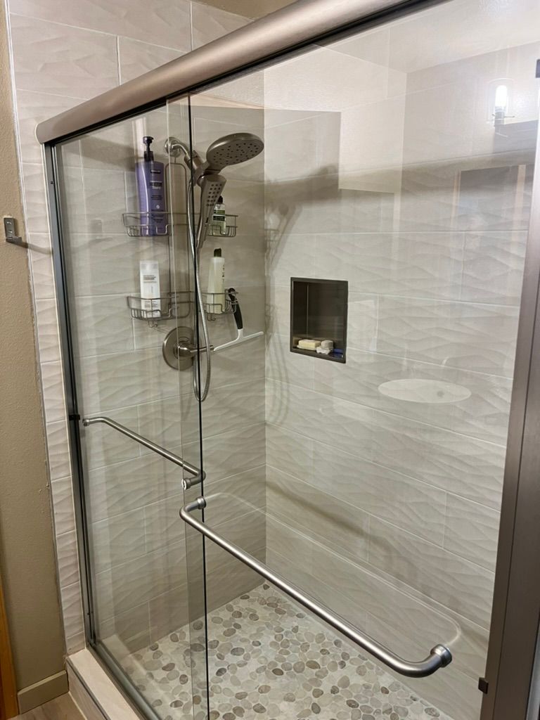 Glass-enclosed shower with stone floor, built-in shelves, and grab bars in a neutral-toned bathroom.